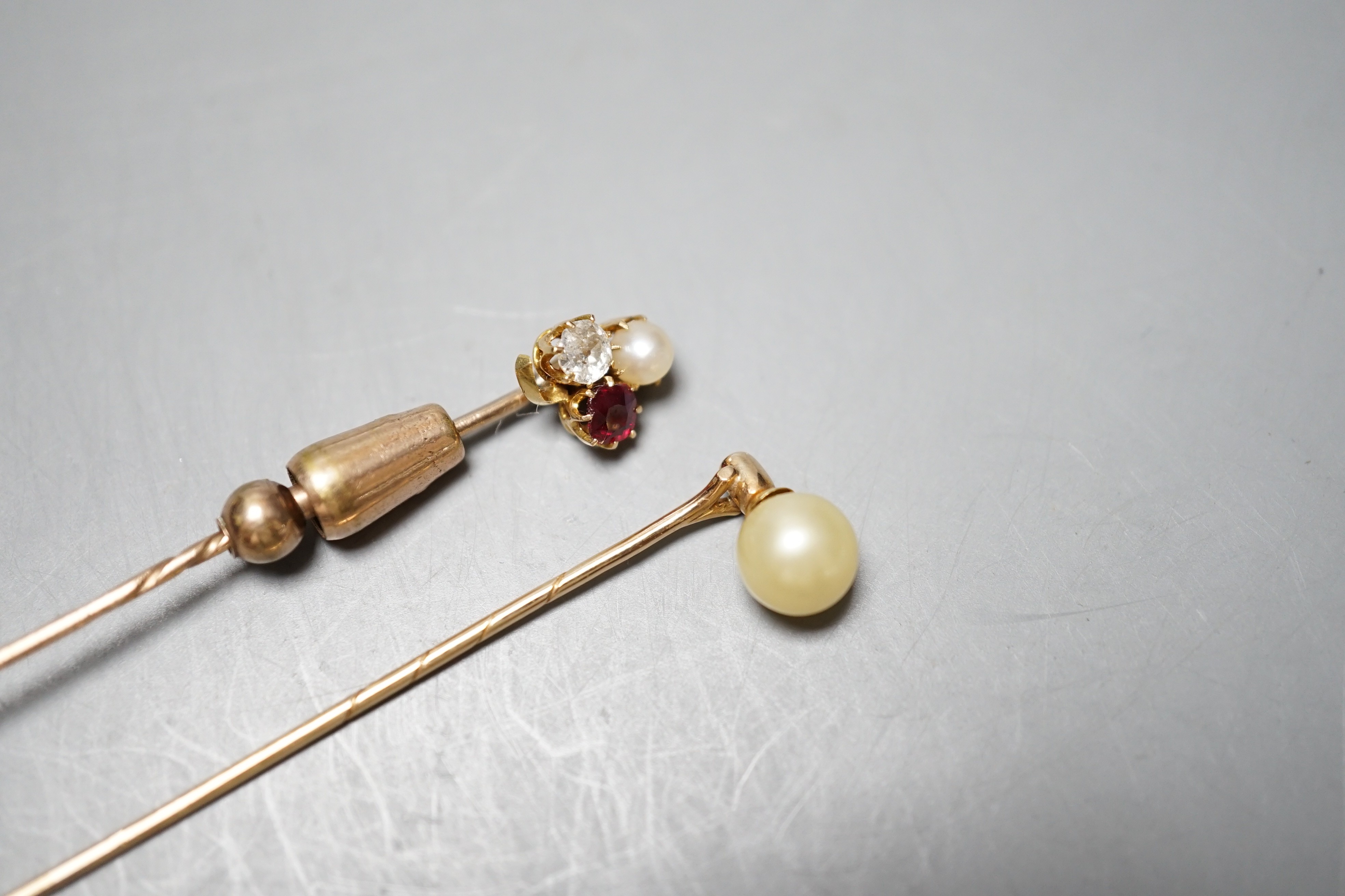 An early 20th century yellow metal, ruby, diamond and cultured pearl cluster set stick pin, 58mm and a yellow metal and simulated pearl stick pin.